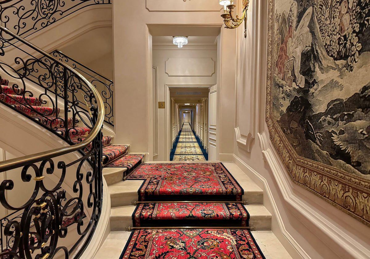 A grand staircase and hallway inside the Ritz Paris, lined with its own tapestries and carpets.