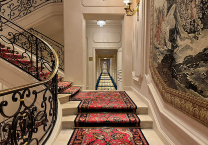 A grand staircase and hallway inside the Ritz Paris, lined with its own tapestries and carpets.