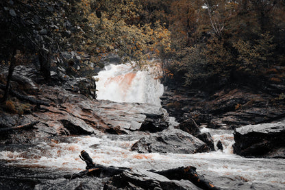 A burn falling white over dark rock between autumn trees.