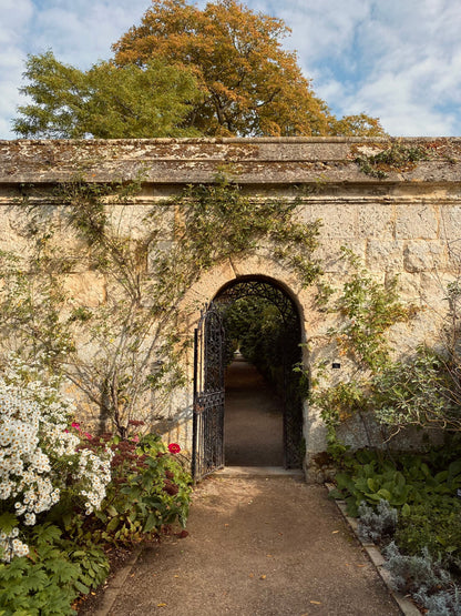 An iron gate opens through a golden stone wall into a walled garden, an evocative image for the Medieval Herb Garden at The Spa at The Newt in Somerset