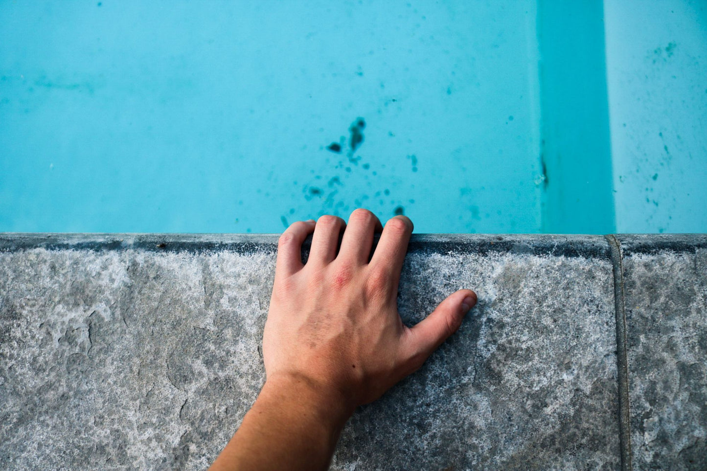 A hand resting on the stone edge of the pool at The Cross Bath
