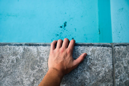 A hand resting on the stone edge of the pool at The Cross Bath