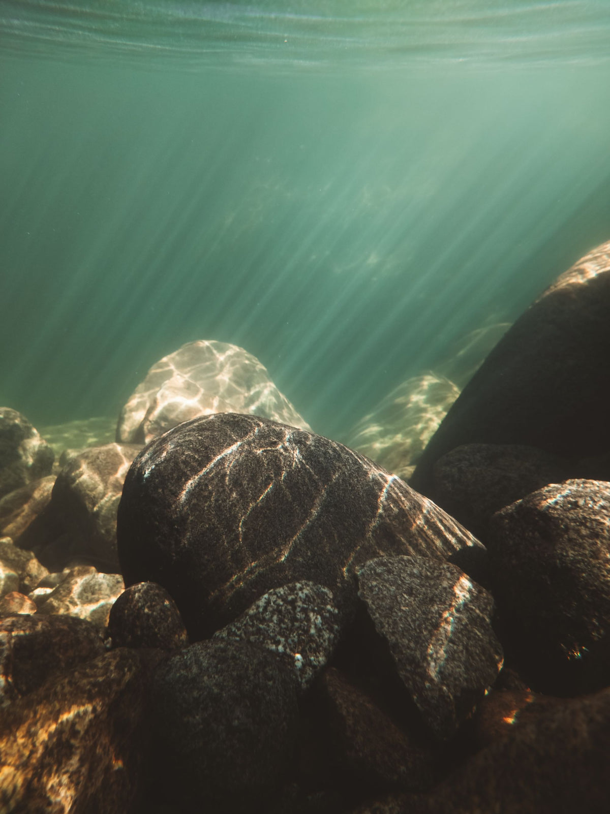 Light rays through clear water over stones, evoking the warm saltwater bath at the heart of the Bathhouse