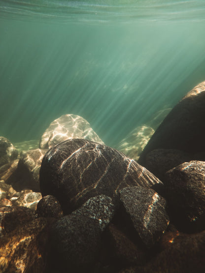 Light rays through clear water over stones, evoking the warm saltwater bath at the heart of the Bathhouse