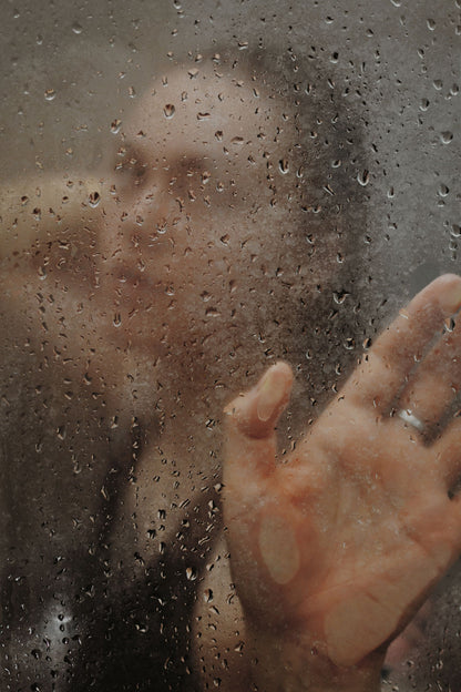 A hand against a rain streaked glass wall, evoking the walk through rainforest shower