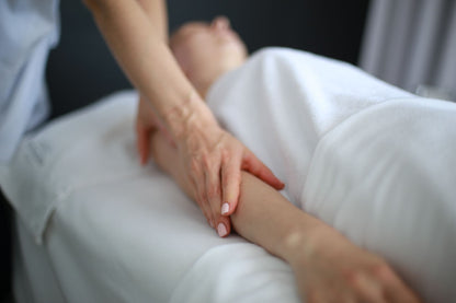 A therapist's hands working on a guest's arm during a treatment, wrapped in white linen
