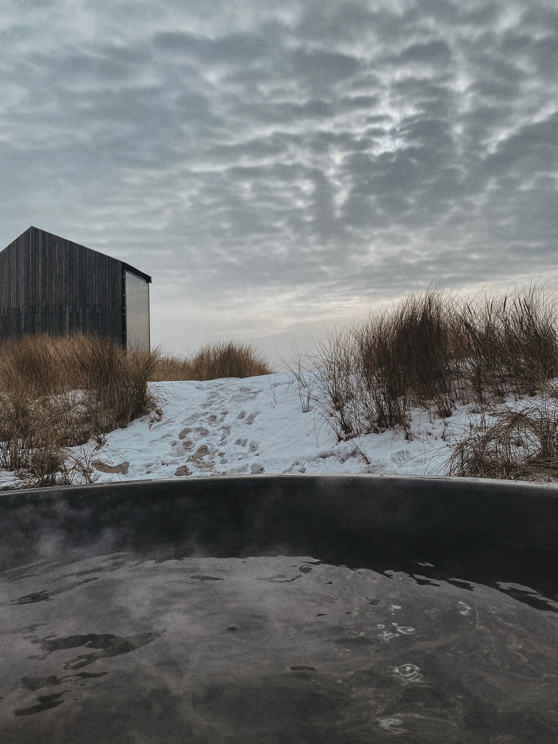 Steam rising off dark bathing water outdoors in winter, The Cowshed Spa at Soho Farmhouse