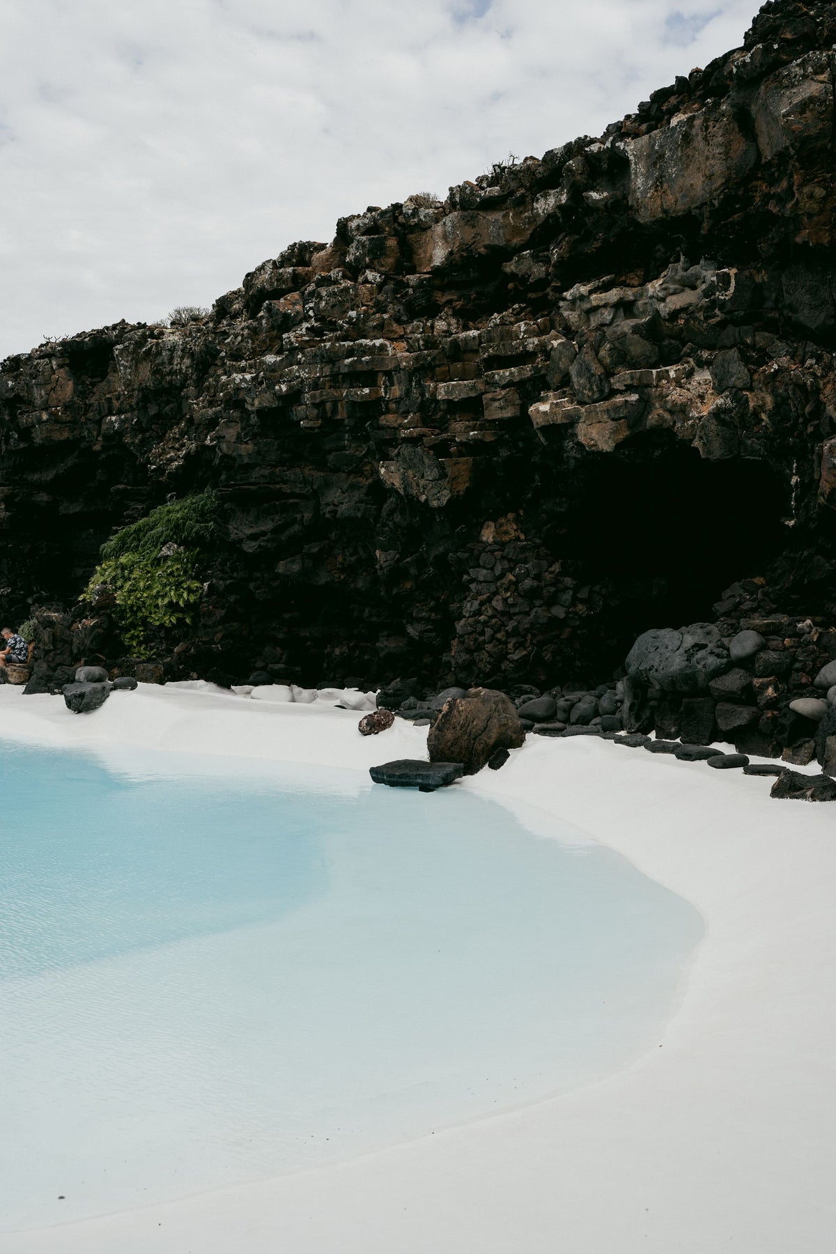 Turquoise water and white sand beneath a rocky cove, evoking the light and colour of the Isles of Scilly coastline.