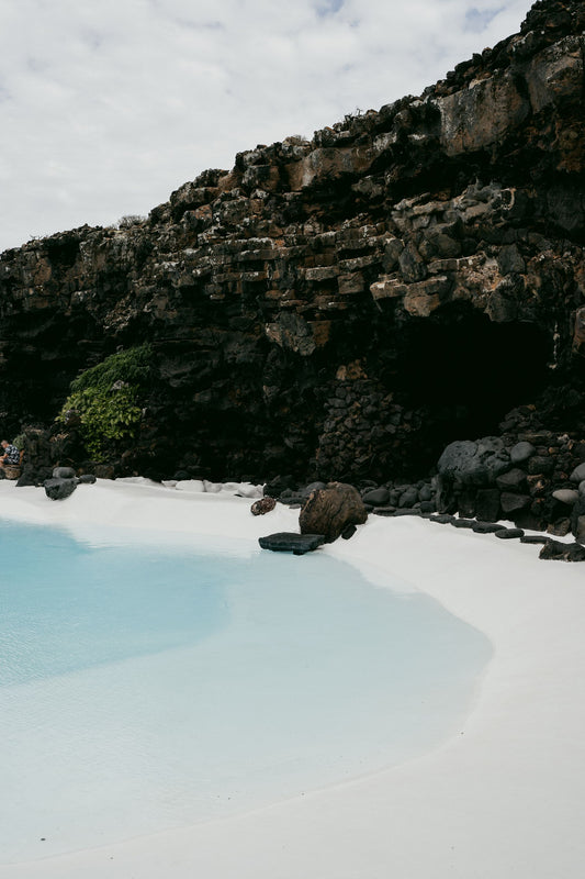 Turquoise water and white sand beneath a rocky cove, evoking the light and colour of the Isles of Scilly coastline.