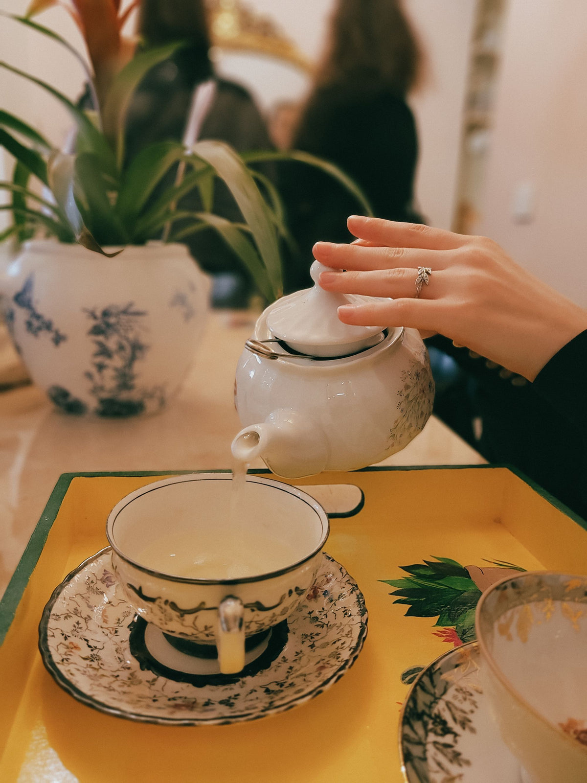 A hand pouring tea from a porcelain teapot
