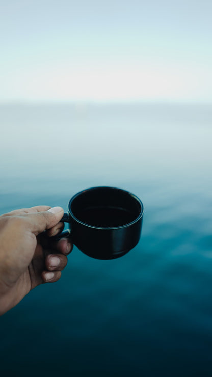 Hand holding a warm mug against a blue sea horizon near The Scarlet Spa, Mawgan Porth