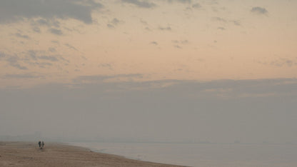 Two figures walking a misty beach at dawn