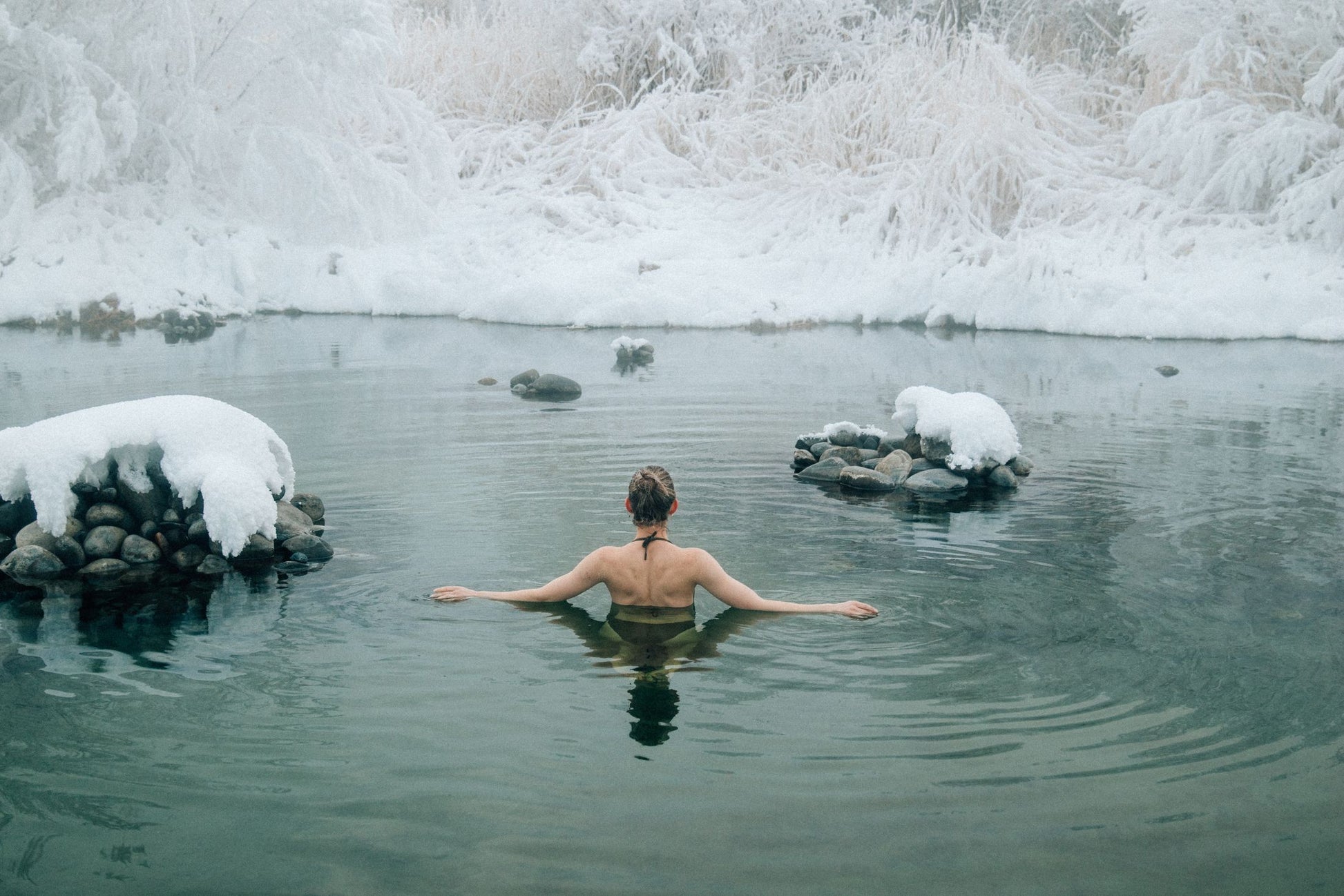 A bather resting in cold green water between snow covered rocks, The Cowshed Spa at Soho Farmhouse