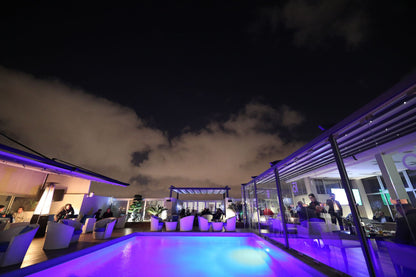 A rooftop pool glowing under night lighting, evoking the mood of a poolside thermal suite