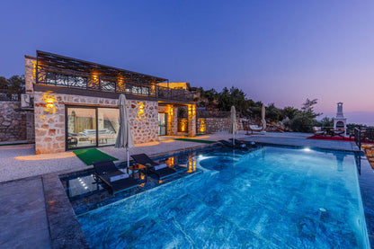 A stone villa with an infinity edge pool glowing with warm light at dusk