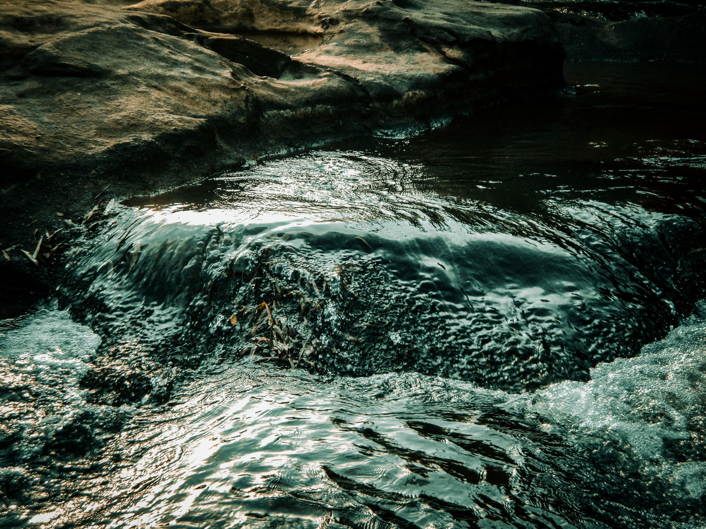 Cold spring water running clear over dark rock, The Meadow Spa at Thyme, Southrop