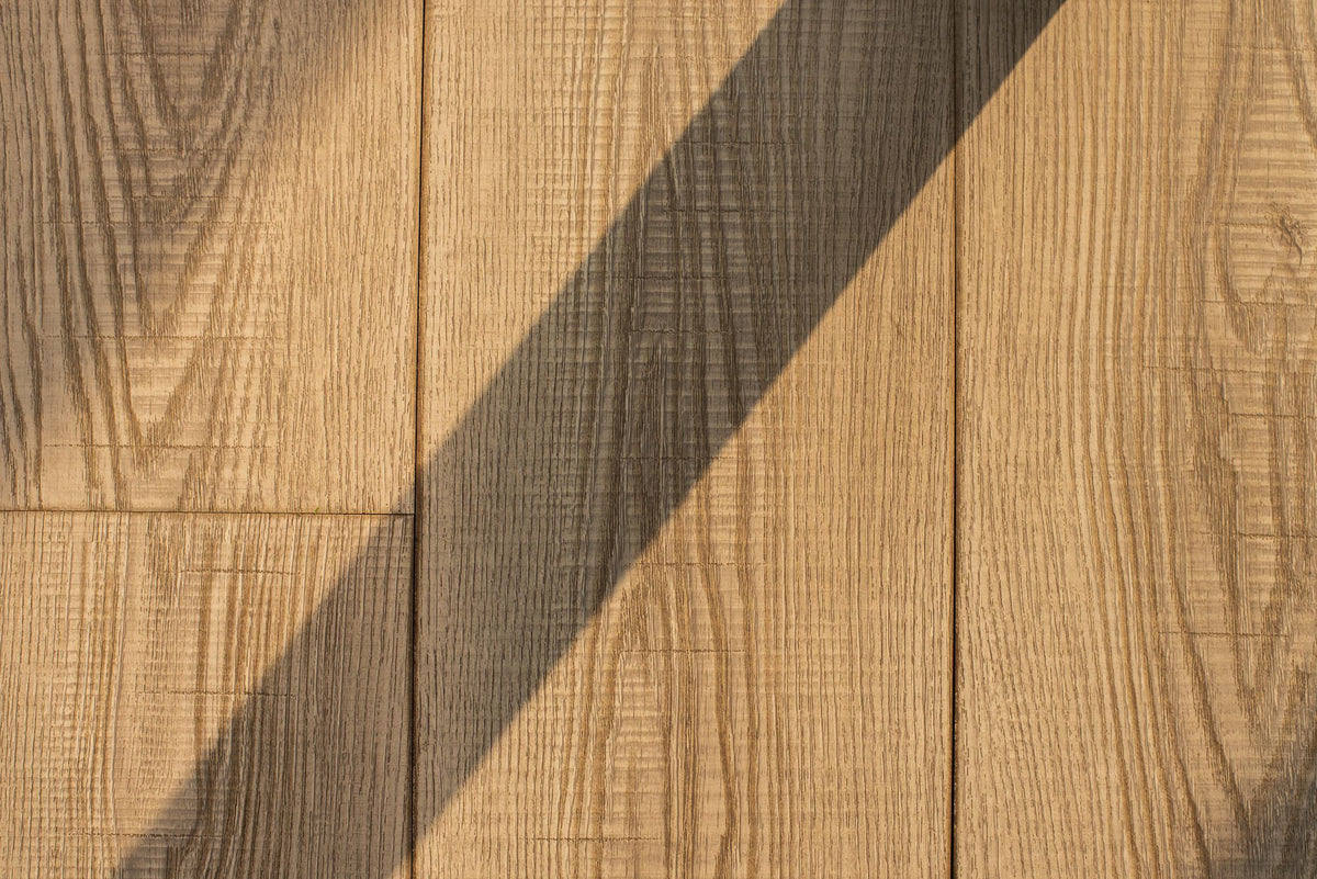 Close detail of honey toned wood grain, a diagonal shadow falling across the planks.