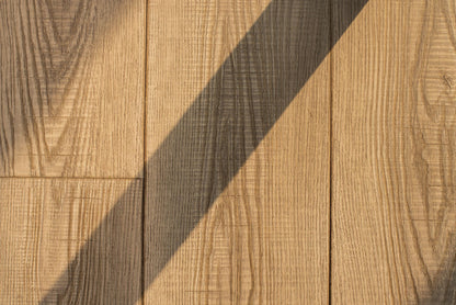 Close detail of honey toned wood grain, a diagonal shadow falling across the planks.