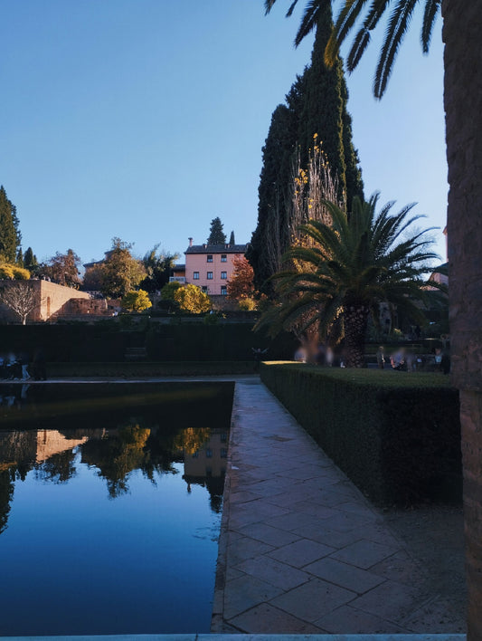 A reflective garden pool bordered by clipped hedges and cypress trees, evoking the gardens at Borgo Santo Pietro.
