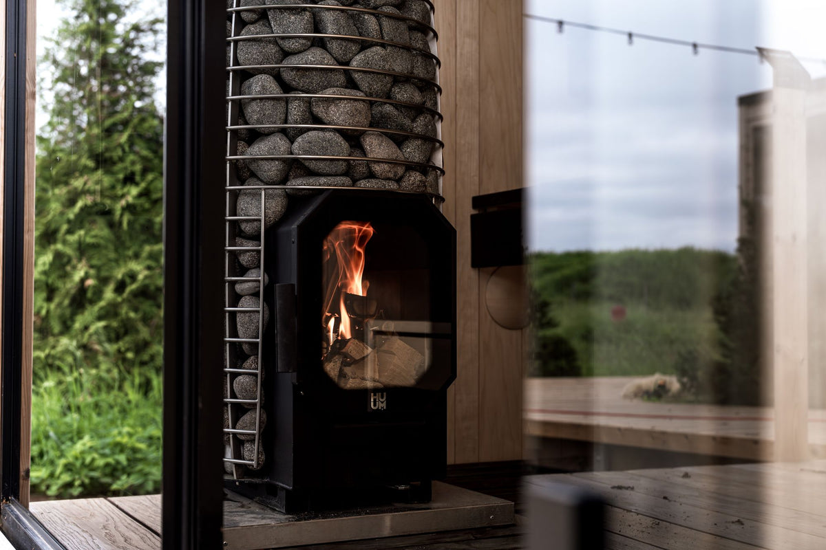 A stylish sauna interior with a modern stone heater and a view of lush greenery