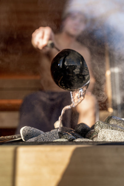 Water poured over hot sauna stones releasing steam in a wood lined sauna