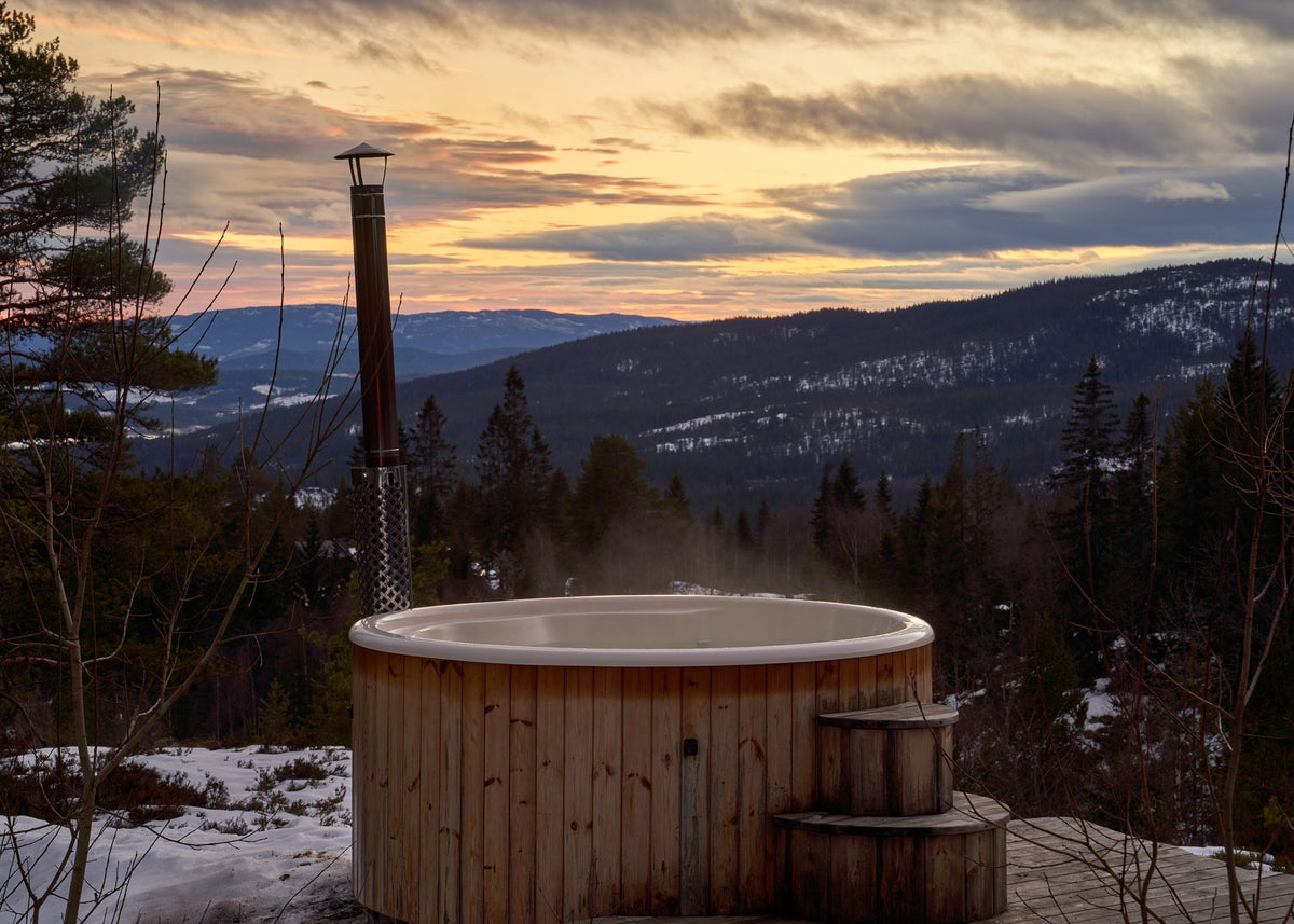 A wooden hot tub steams on a deck at dusk, hills rolling away into the distance.