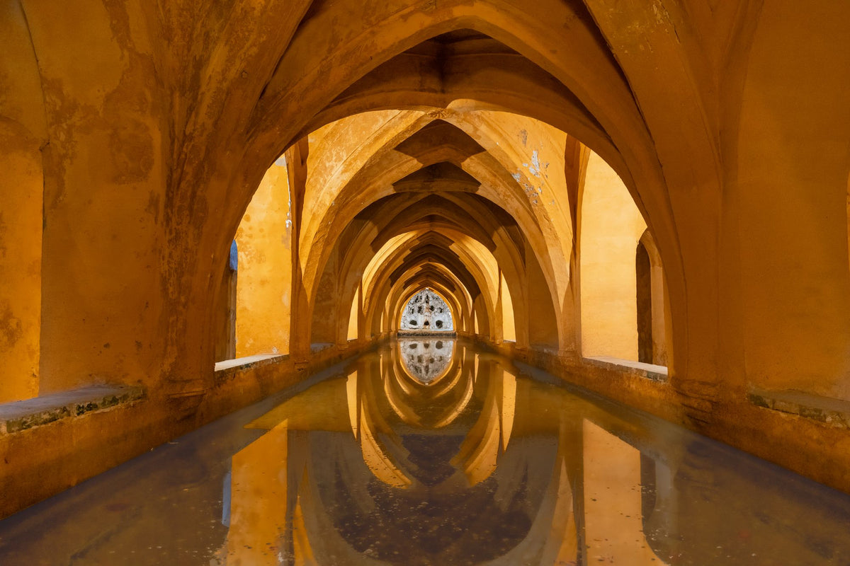 Reflective arched stone baths at the Alcazar of Sevilla, evoking the hacienda's historic character