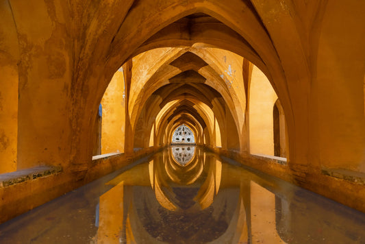 Reflective arched stone baths at the Alcazar of Sevilla, evoking the hacienda's historic character