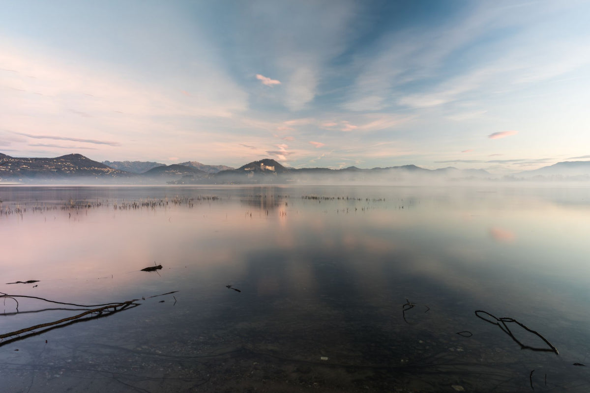 A misty sunrise over a calm lake with mountains in the distance