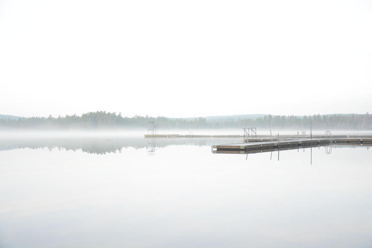 A tranquil misty lake at dawn with a wooden dock extending into the fog