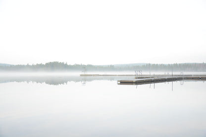 A tranquil misty lake at dawn with a wooden dock extending into the fog