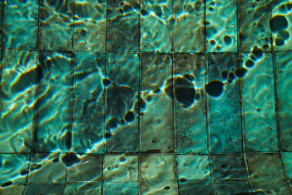 Close up of teal green mosaic pool tiles under rippling water