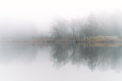 A still lake reflects bare trees in cool morning mist.