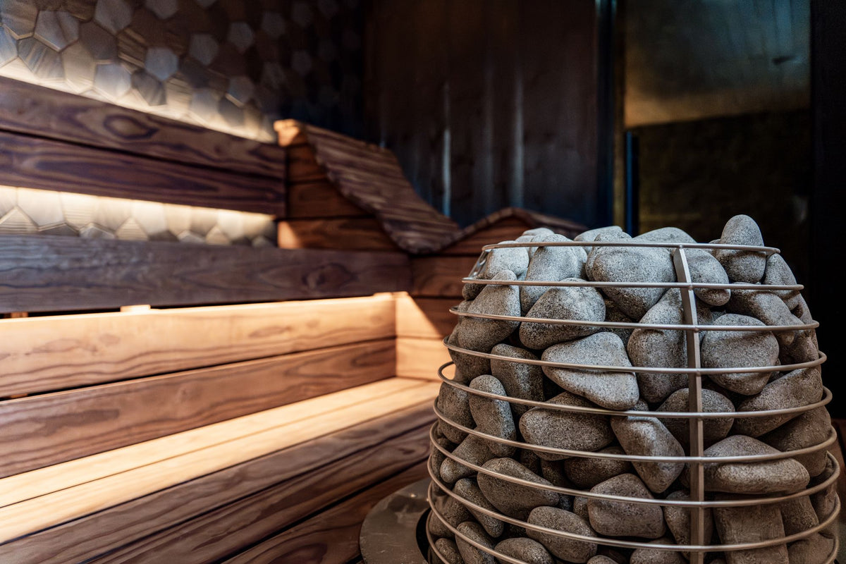 A dark wood sauna interior lit with warm light, with a bowl of hot stones