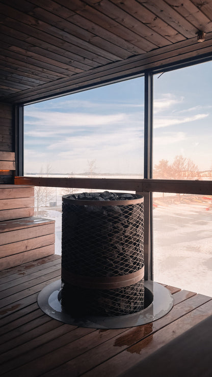 A wood panelled sauna with a heater beside a large window looking out over a winter landscape