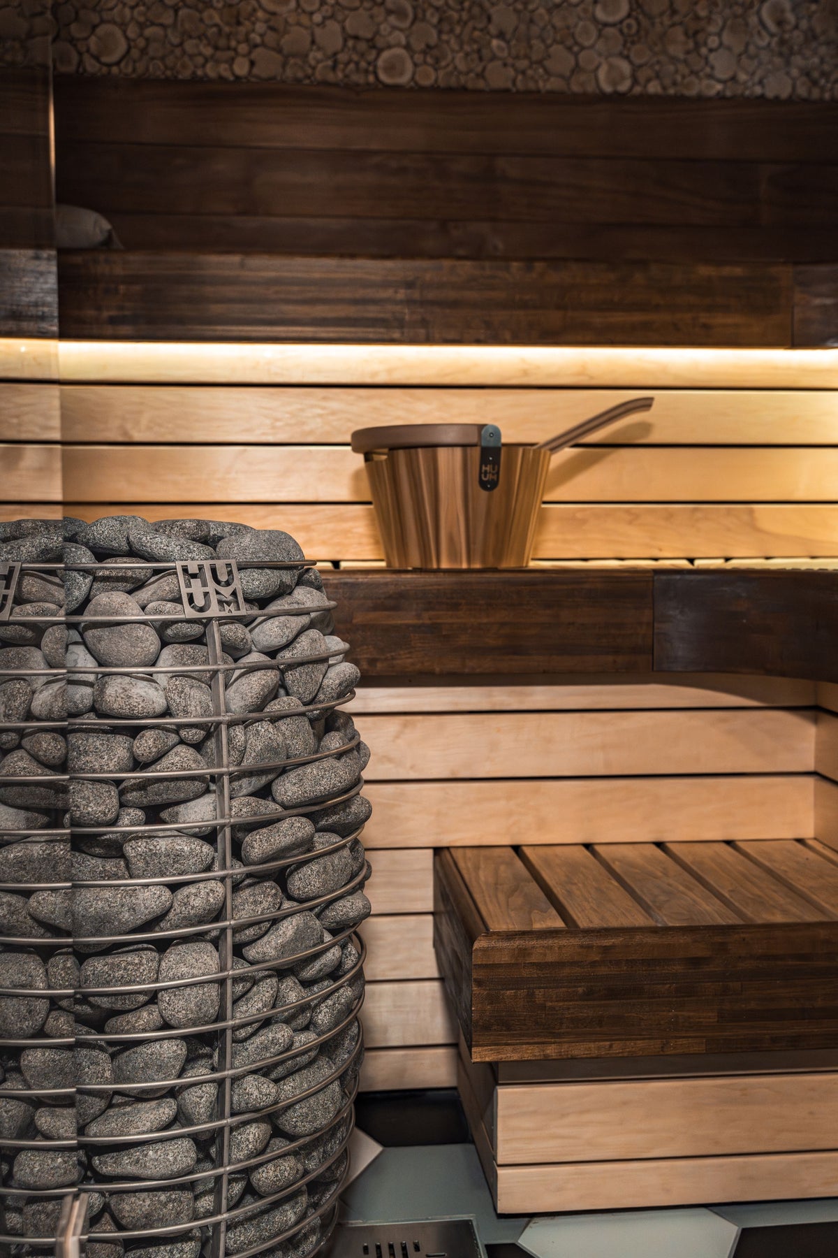 Warm wood sauna interior with a stone heater glowing low, the heat experience at the heart of a small recovery club