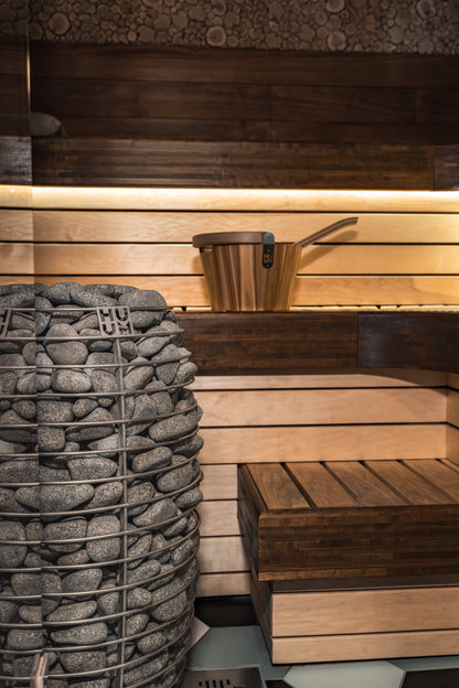 Warm wood sauna interior with a stone heater glowing low, the heat experience at the heart of a small recovery club