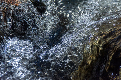Close up of cold rushing water over dark rock, evoking a cold water plunge