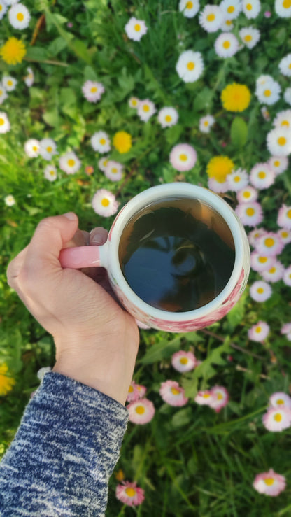 A hand holding a cup of herbal tea among wildflowers