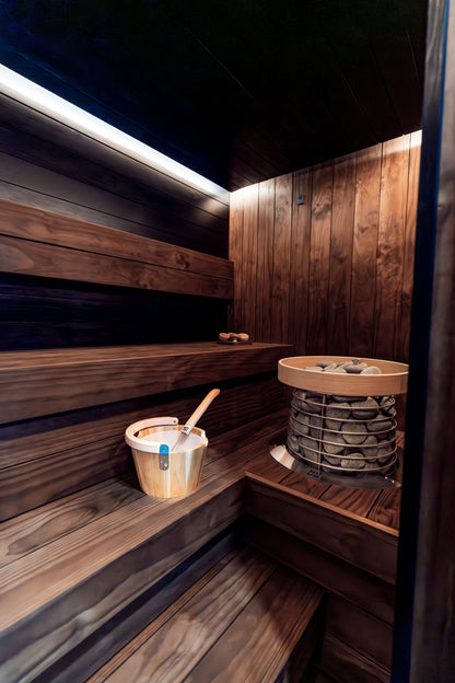 Warm light and heated stones inside a dark wood sauna, The Bothy by Wildsmith at Heckfield Place
