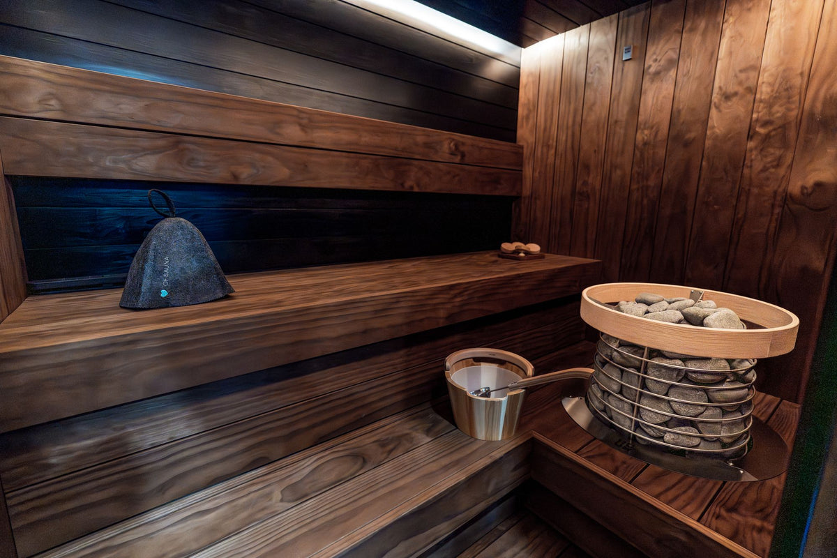 A dark wood sauna interior with warm low lighting and a heater filled with stones