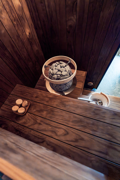 A dark timber sauna with hot stones banked in the heater, the heat at Asaya at The Chancery Rosewood