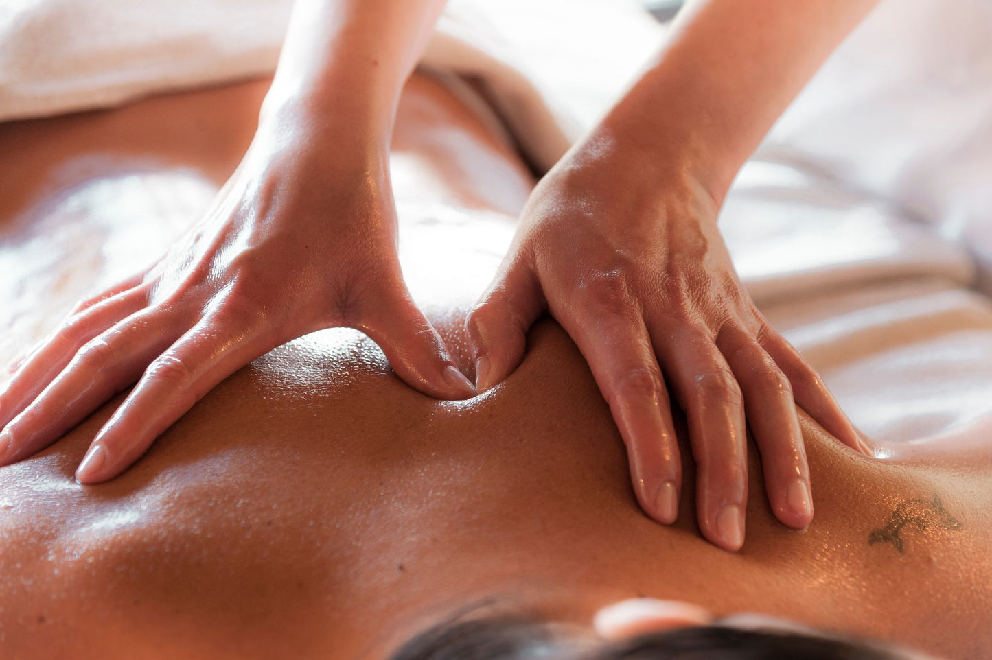 A therapist's hands working warm oil into a guest's back