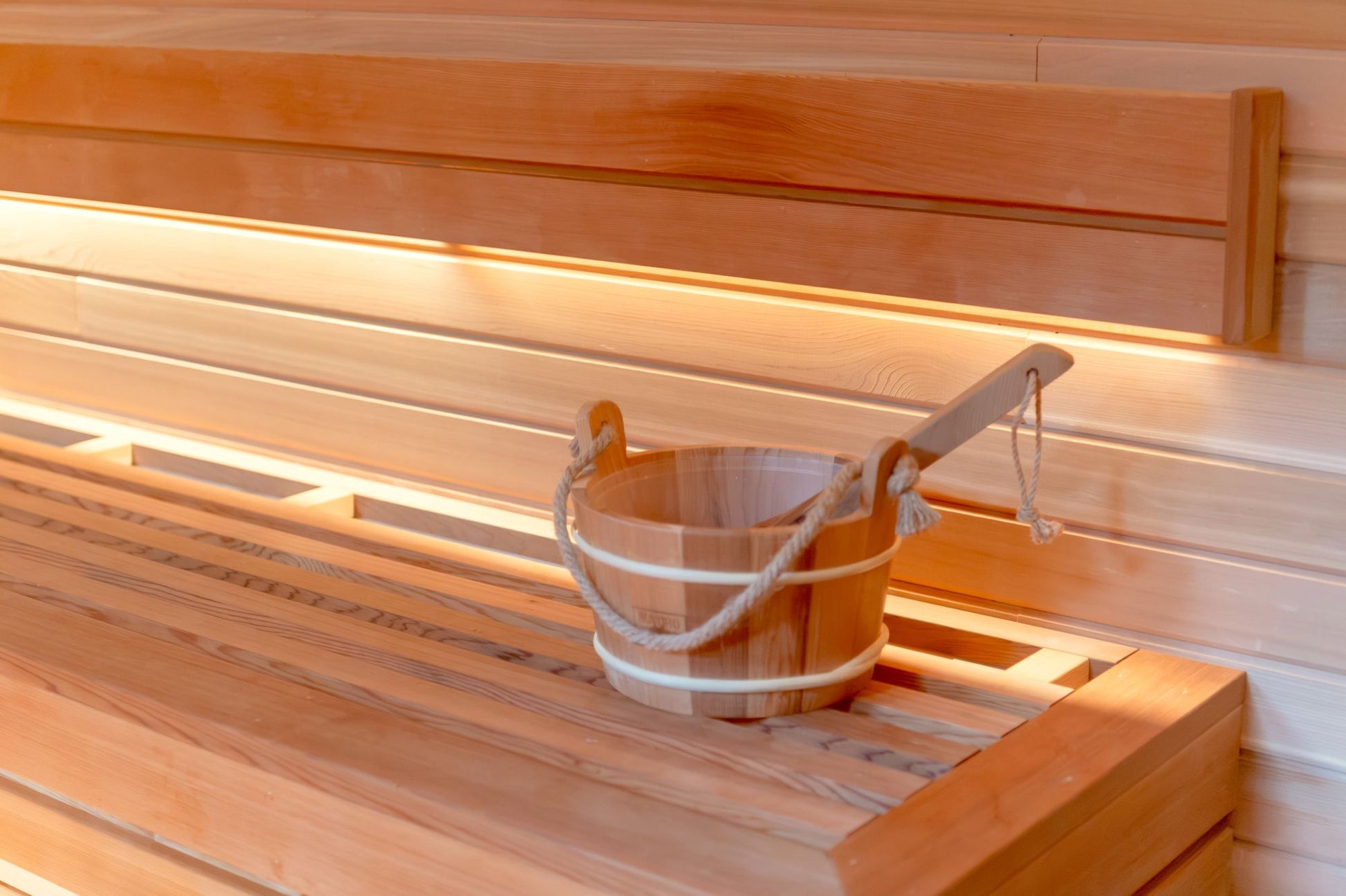 A wooden pail and ladle set on a sauna bench in warm light, the heat at The Bvlgari Spa, Knightsbridge