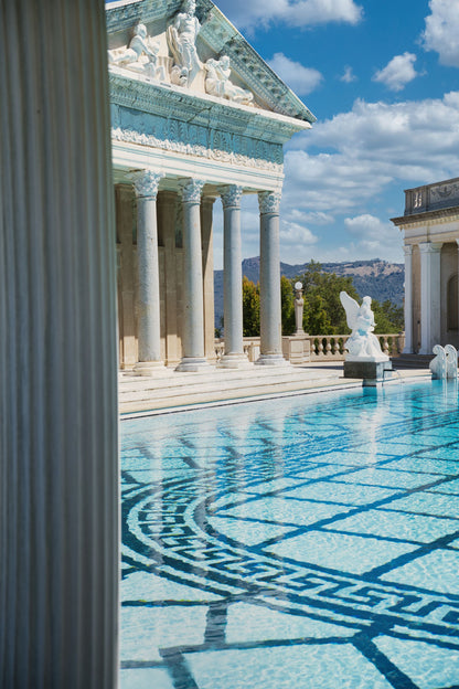 Sunlit marble columns and mosaic tiled water beside a grand classical pool.