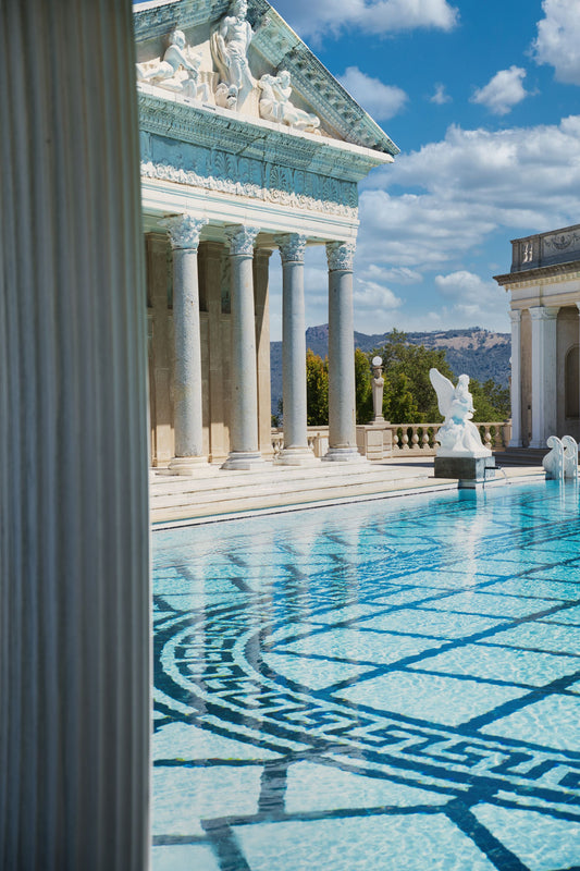 Sunlit marble columns and mosaic tiled water beside a grand classical pool.