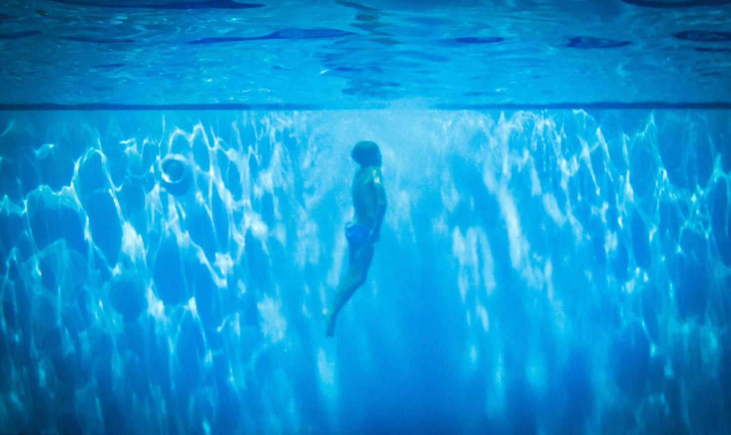 A swimmer suspended underwater in blue light, evoking a swim in the skylit pond