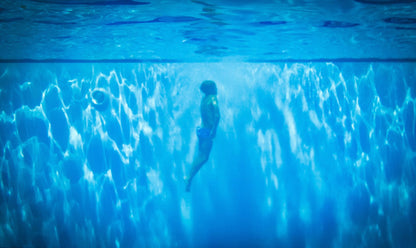 A swimmer suspended underwater in blue light, evoking a swim in the skylit pond