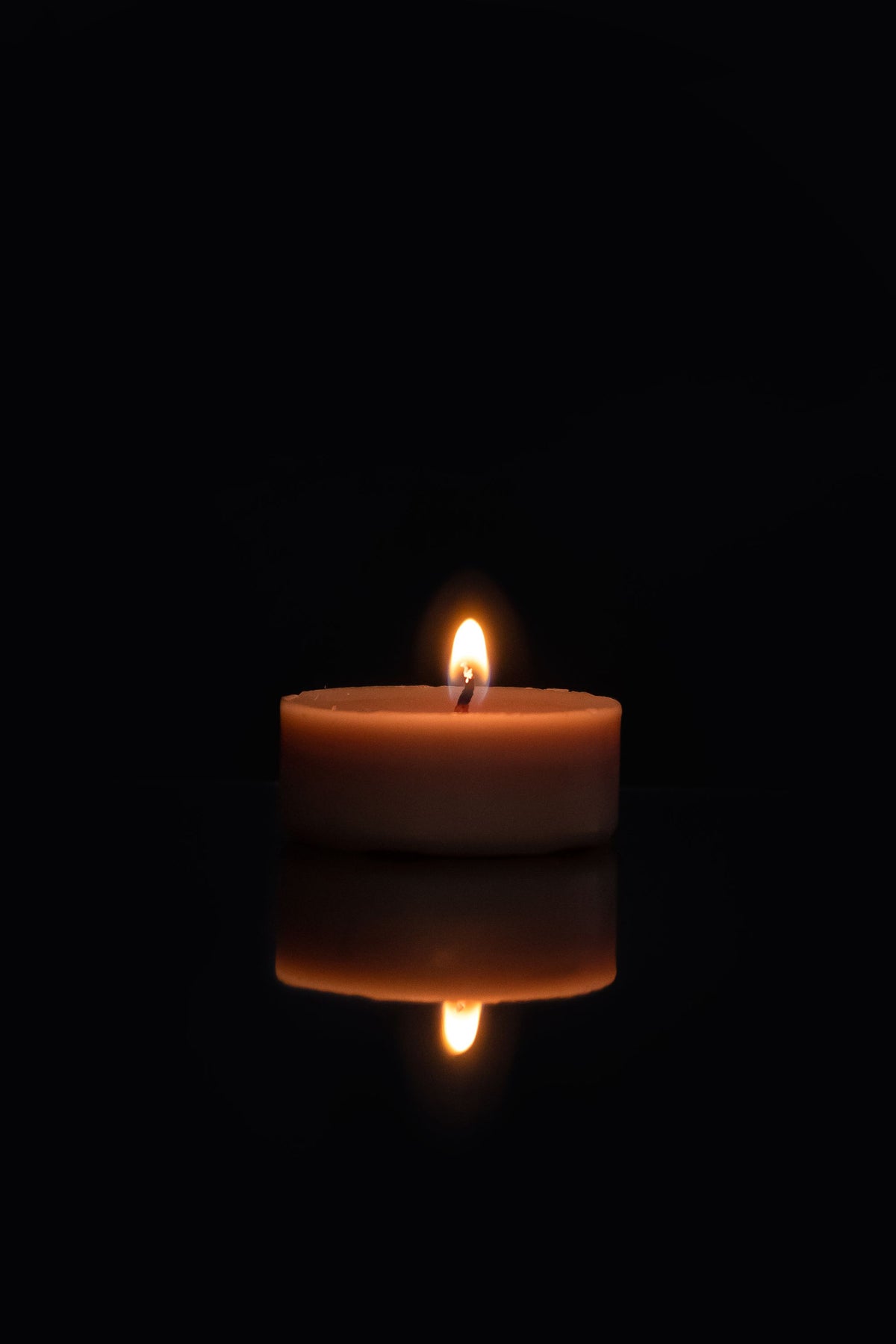 A single candle flame in darkness, evoking the warmth of a Seed to Skin candle massage.
