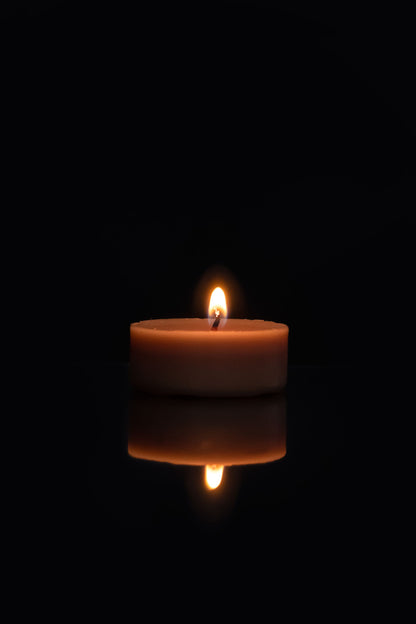 A single candle flame in darkness, evoking the warmth of a Seed to Skin candle massage.